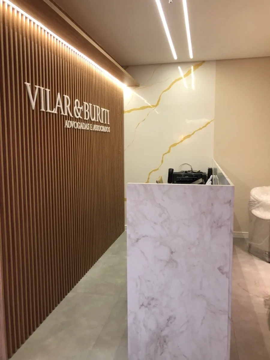 Recepção do escritório Vilar & Buriti, com painel ripado iluminado por fita de luz e balcão claro